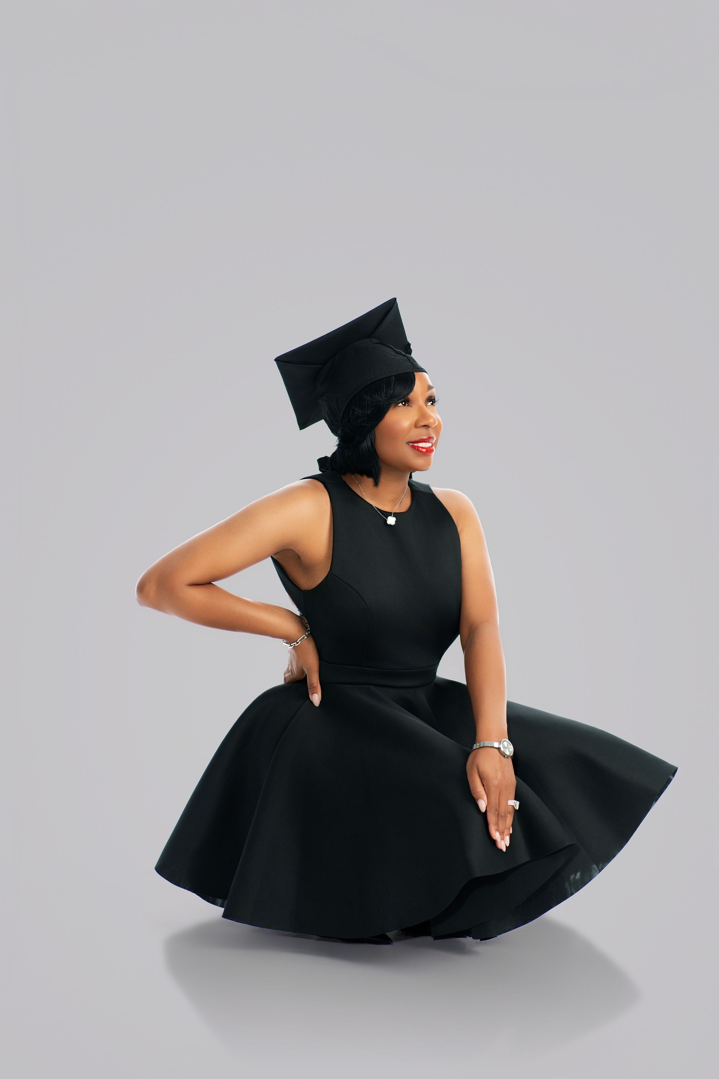 Young woman in black dress and graduation cap posing gracefully, celebrating academic achievement.