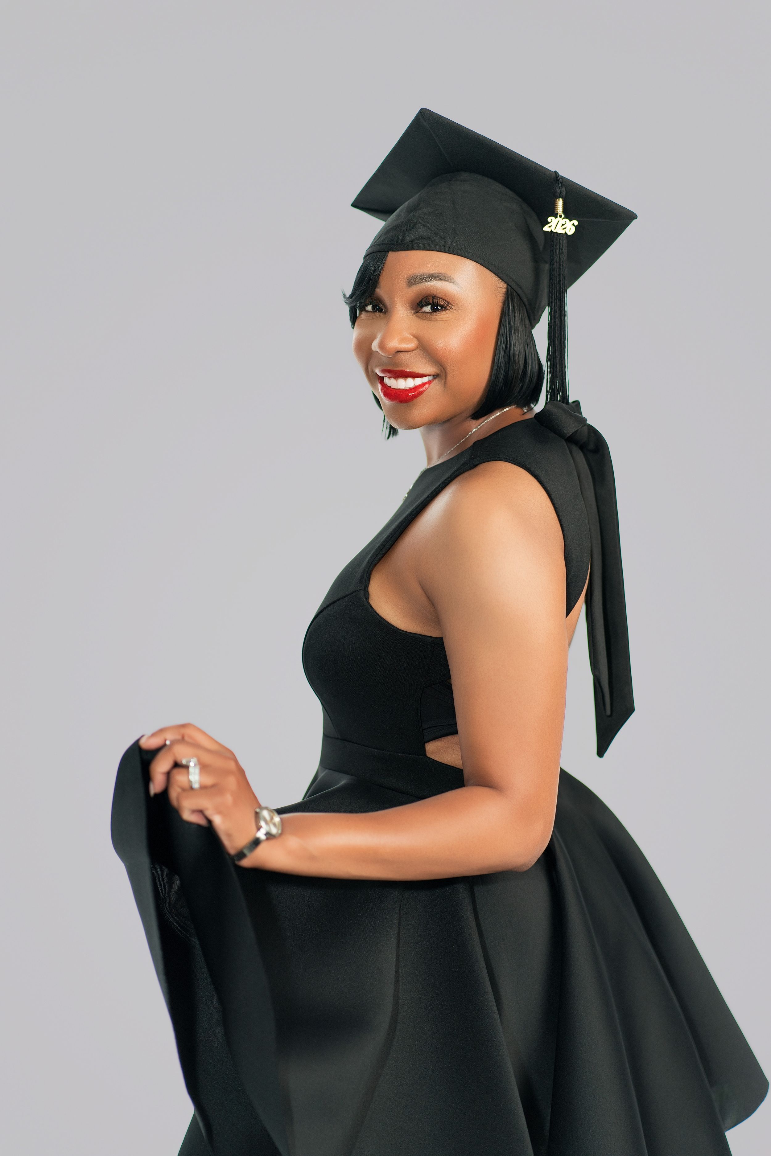 Smiling Black woman in black graduation cap and dress posing for a portrait photo.