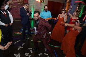 Party guests dancing and celebrating at a reception with colored lighting and brick walls.