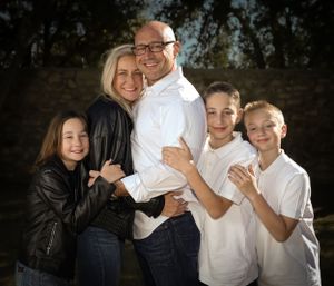 Happy family wearing white and black outfits pose together in a casual outdoor setting.