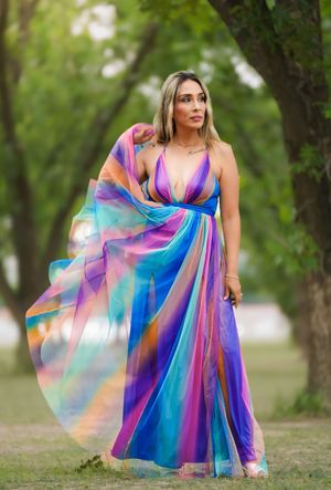 A stunning rainbow-colored flowing maxi dress with vibrant blue, pink and purple hues flows gracefully in an outdoor setting.