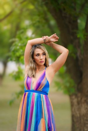 A vibrant rainbow colored maxi dress with halter neckline stands out against a soft green natural outdoor background.