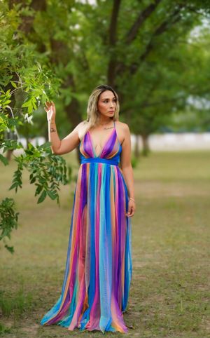 A flowing multicolored striped maxi dress with pink, blue and purple hues photographed against a natural outdoor backdrop.