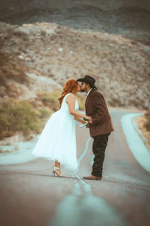 Romantic couple in wedding attire sharing a kiss on a winding mountain road.