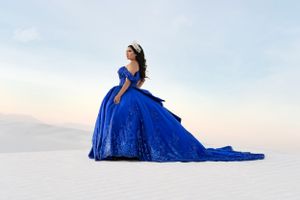 Woman in flowing royal blue ball gown poses dramatically on white sand.