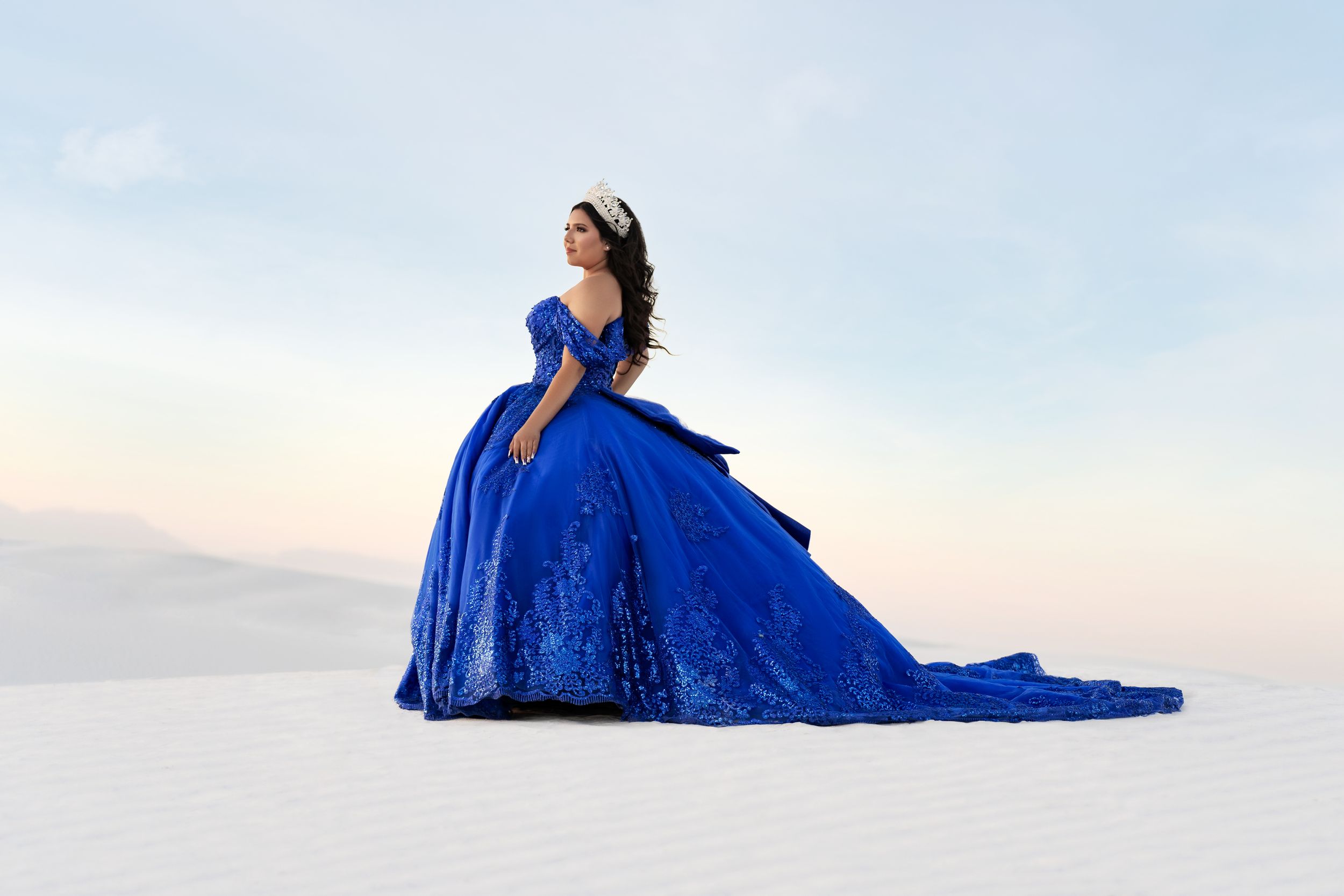 Woman in flowing royal blue ball gown poses dramatically on white sand.