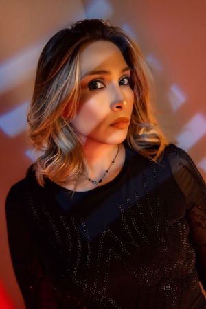 Professional model in black dress poses against warm orange lighting and shadows.