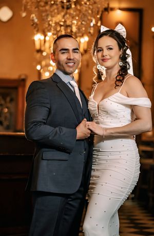 A formal wedding photo showing a couple in elegant attire with twinkle lights and warm lighting in the background.