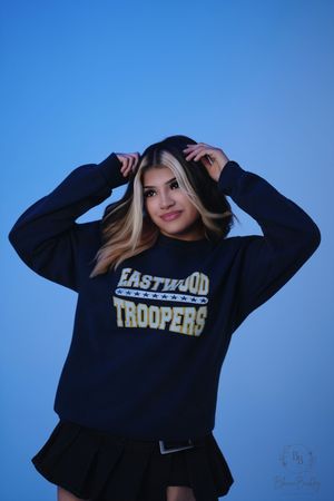 Young woman posing in Eastwood Troopers navy sweatshirt and black skirt against blue background.