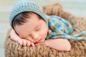 Peaceful newborn baby sleeping in a knit basket wearing a blue striped bonnet hat, perfect for nursery decor inspiration.