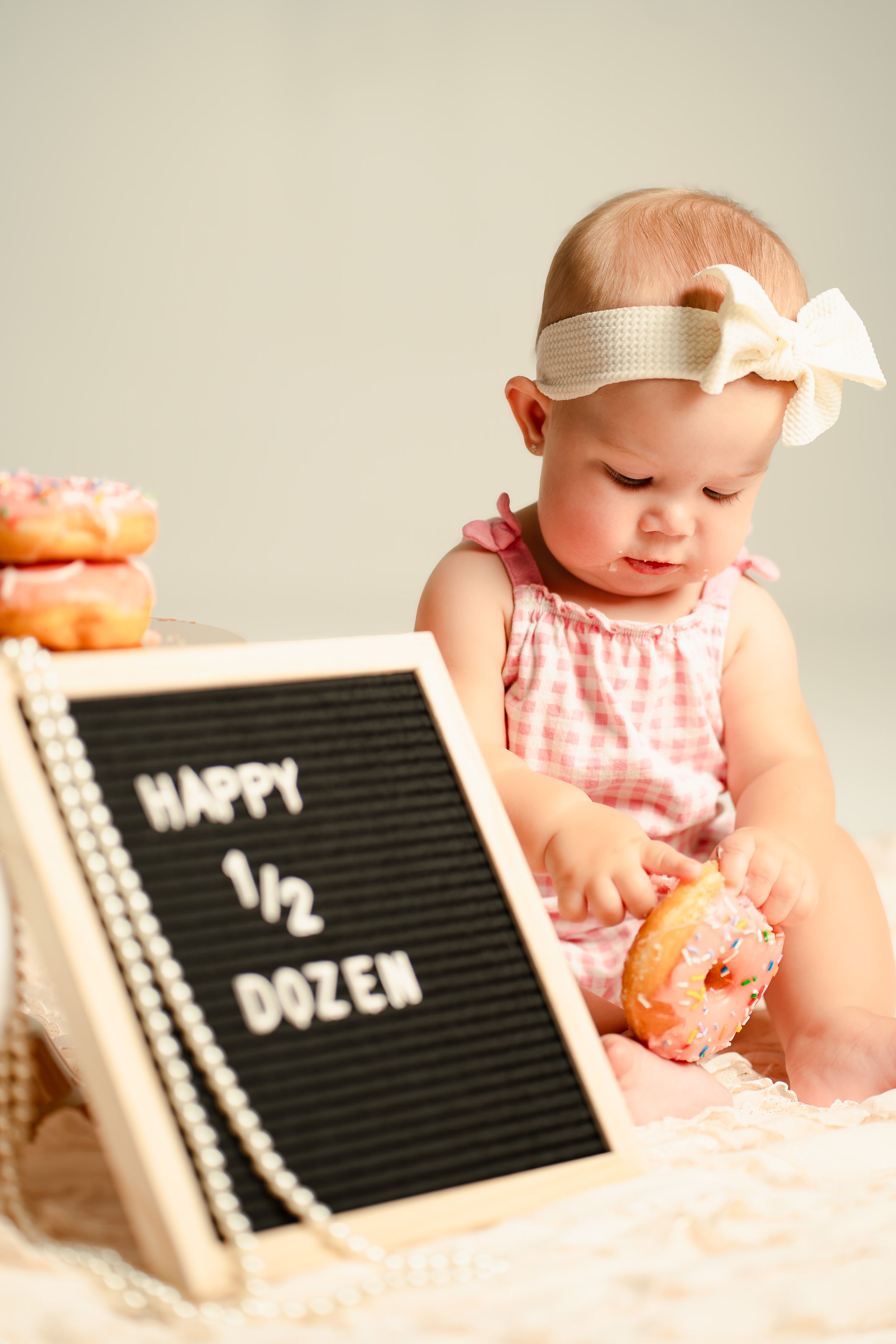Baby girl in pink romper celebrates half birthday with donuts and a Happy Half Dozen letterboard sign.