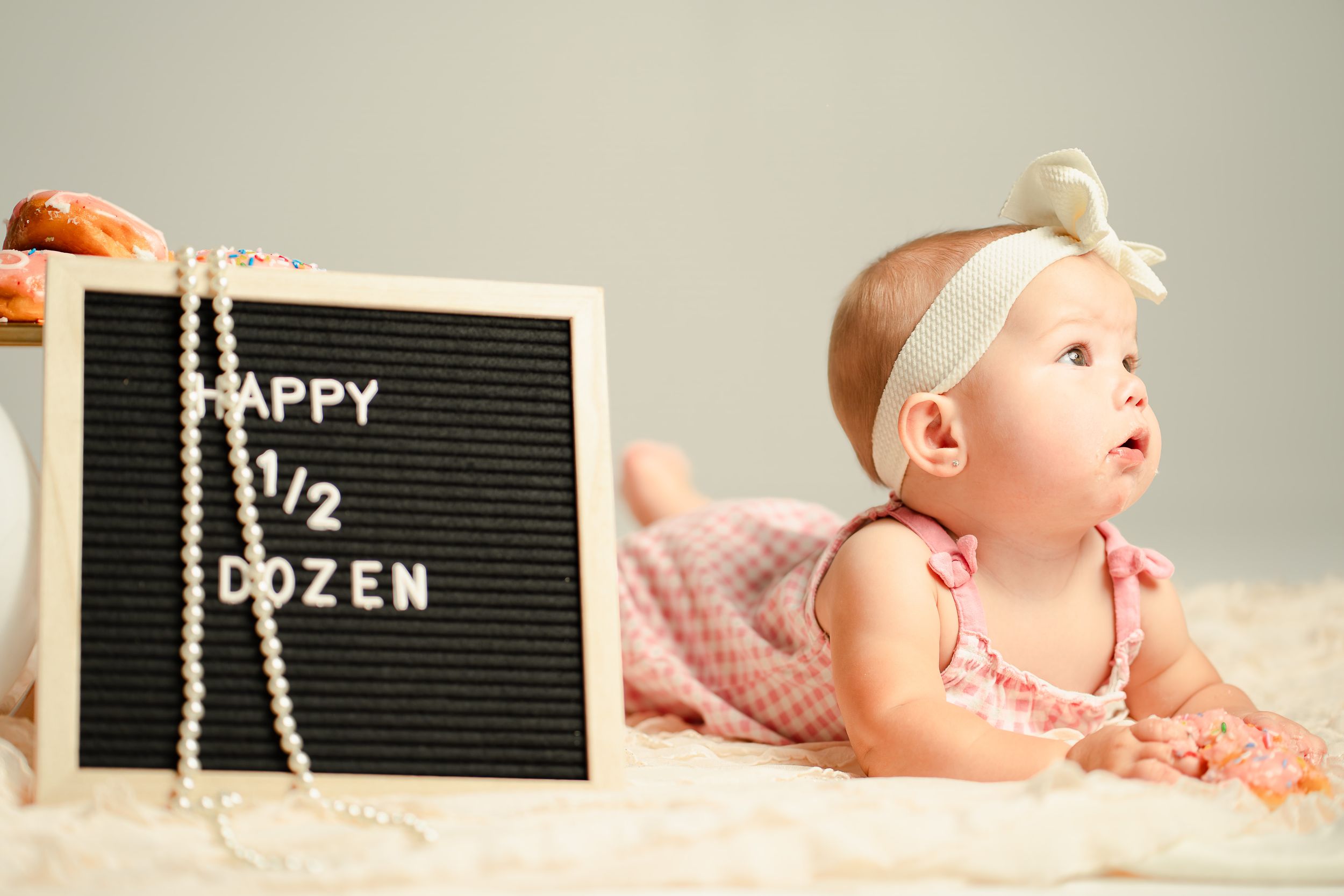 Baby girl in pink dress lying next to a letter board sign reading Happy 1/2 Dozen, celebrating her six-month birthday.