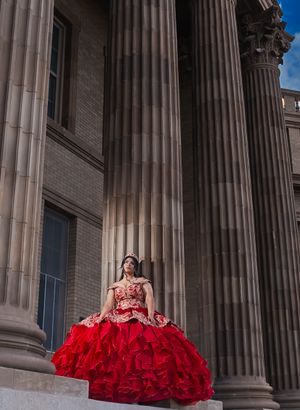 Young woman in red quinceañera dress poses by classical stone columns.