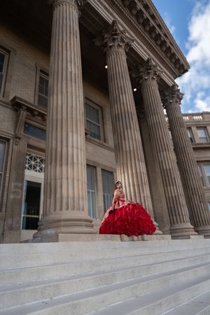 Elegant red ball gown photographed against classical stone columns and marble steps of a grand historic building.