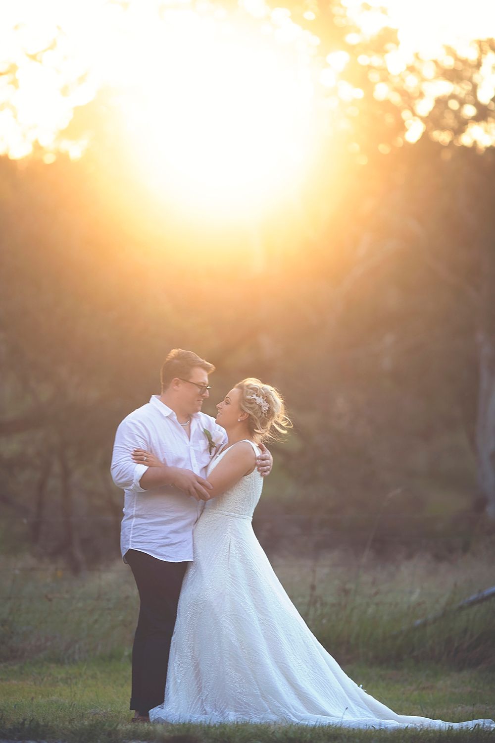 Bride and groom embracing at golden sunset in a lush outdoor setting on their wedding day.