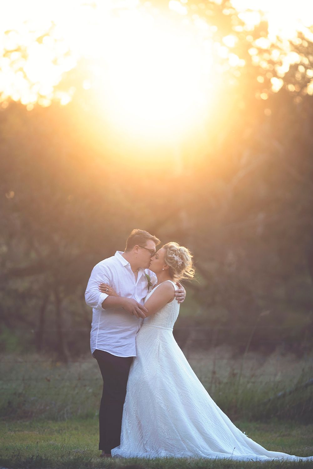 Romantic couple sharing a kiss at sunset, bride in elegant white gown with flowing train.