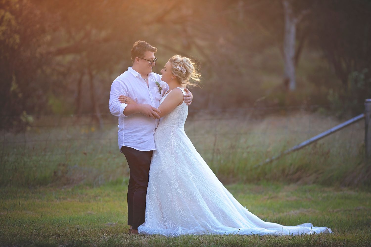 Newlywed couple sharing a tender embrace in a sunlit outdoor setting, bride in white gown.