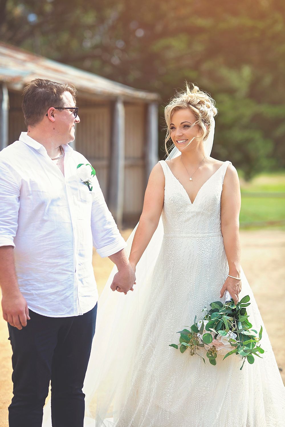 Bride and groom holding hands walking outdoors near rustic barn on their wedding day.