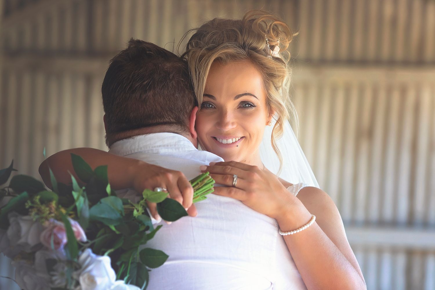 Smiling bride hugging groom while holding a floral bouquet during their wedding celebration.