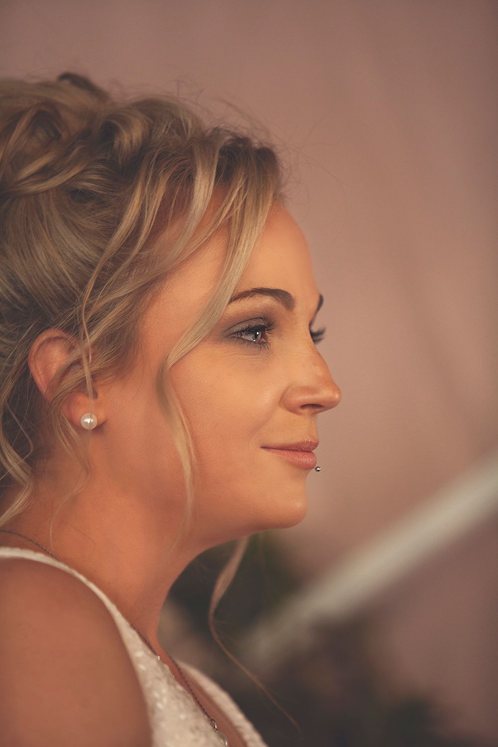 Side profile portrait of a bride with an elegant updo hairstyle and pearl earring on her wedding day.