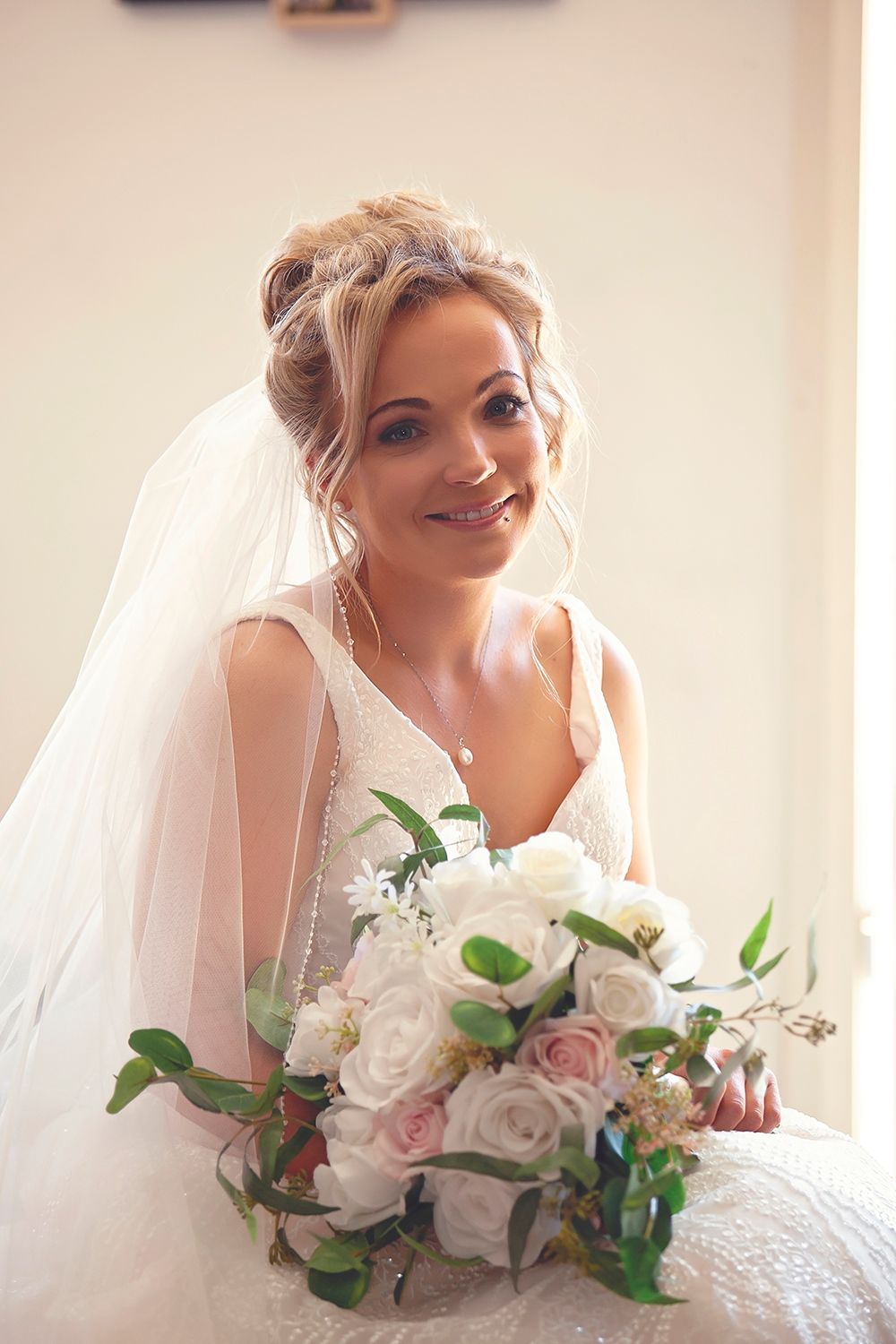 Beautiful bride in white gown and veil holding a bouquet of white and pink roses.