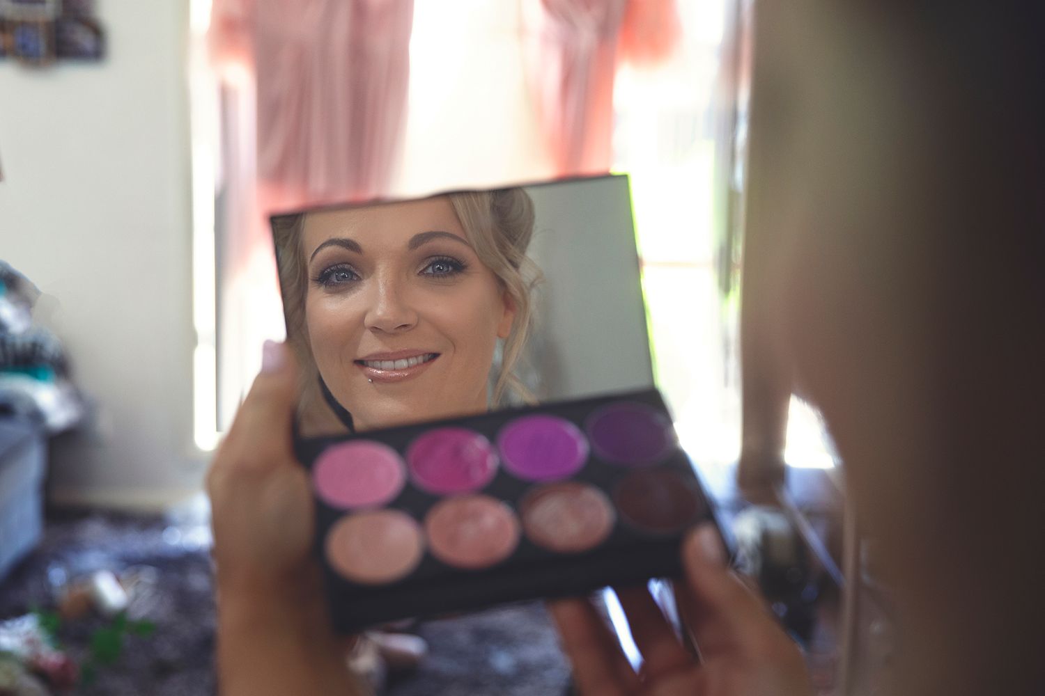 Bride's reflection in a makeup palette mirror during bridal preparations.