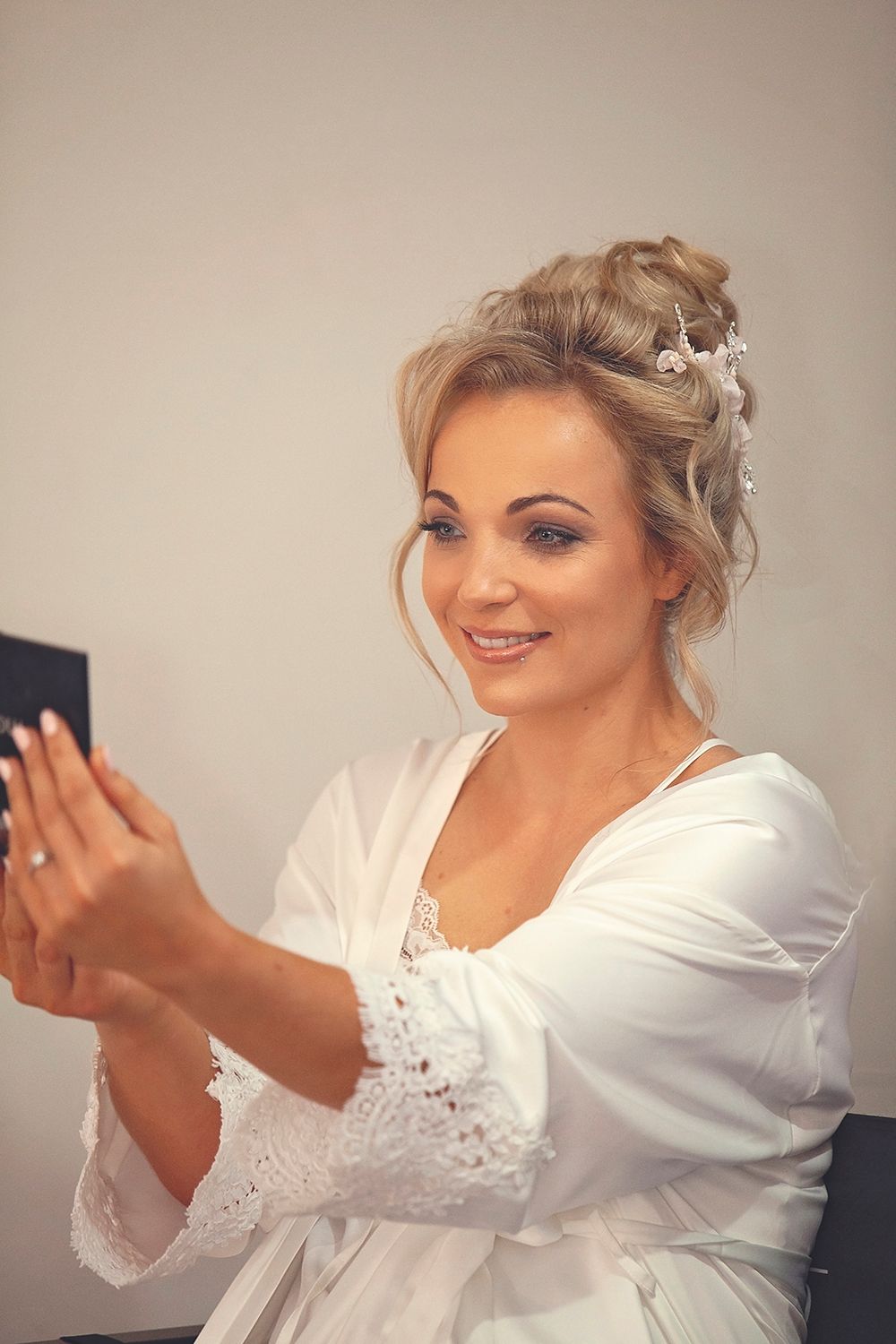 Bride in white robe admiring her engagement ring while getting ready on wedding day.