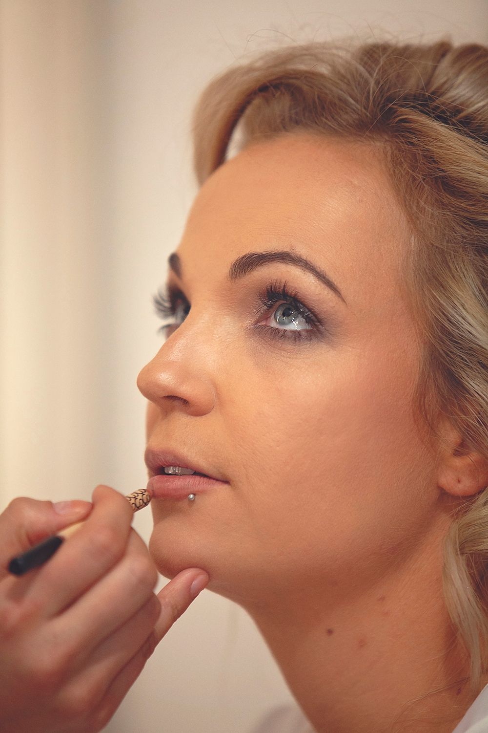 Makeup artist applying lipstick to a blonde bride during wedding day preparations.