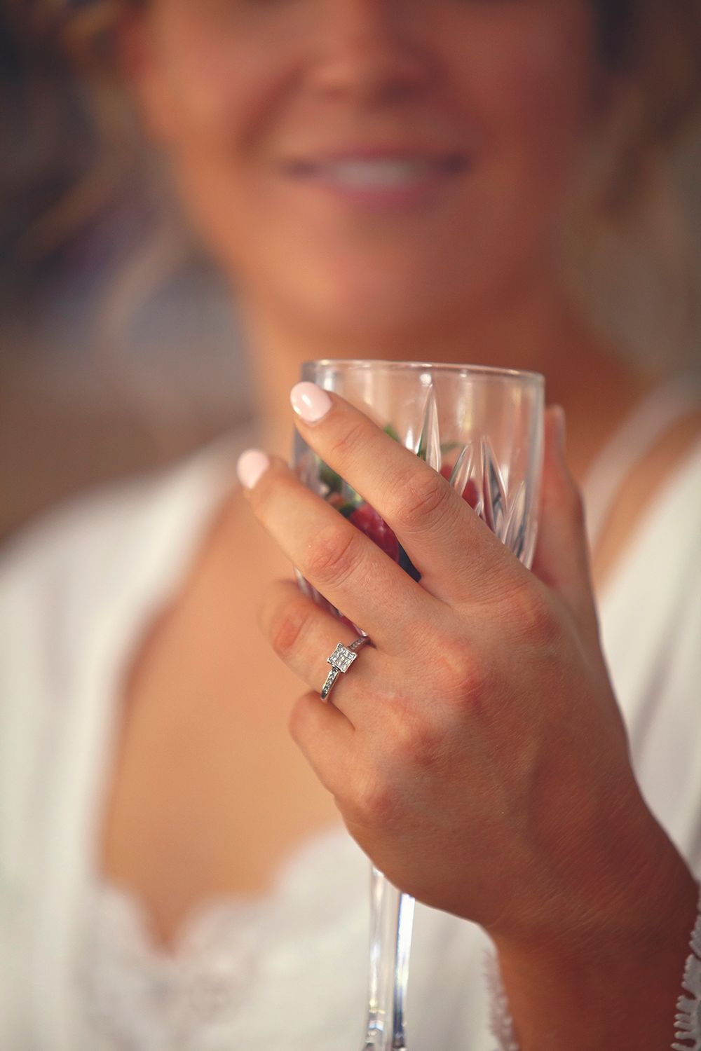 Close-up of bride holding champagne glass with diamond engagement ring on finger.