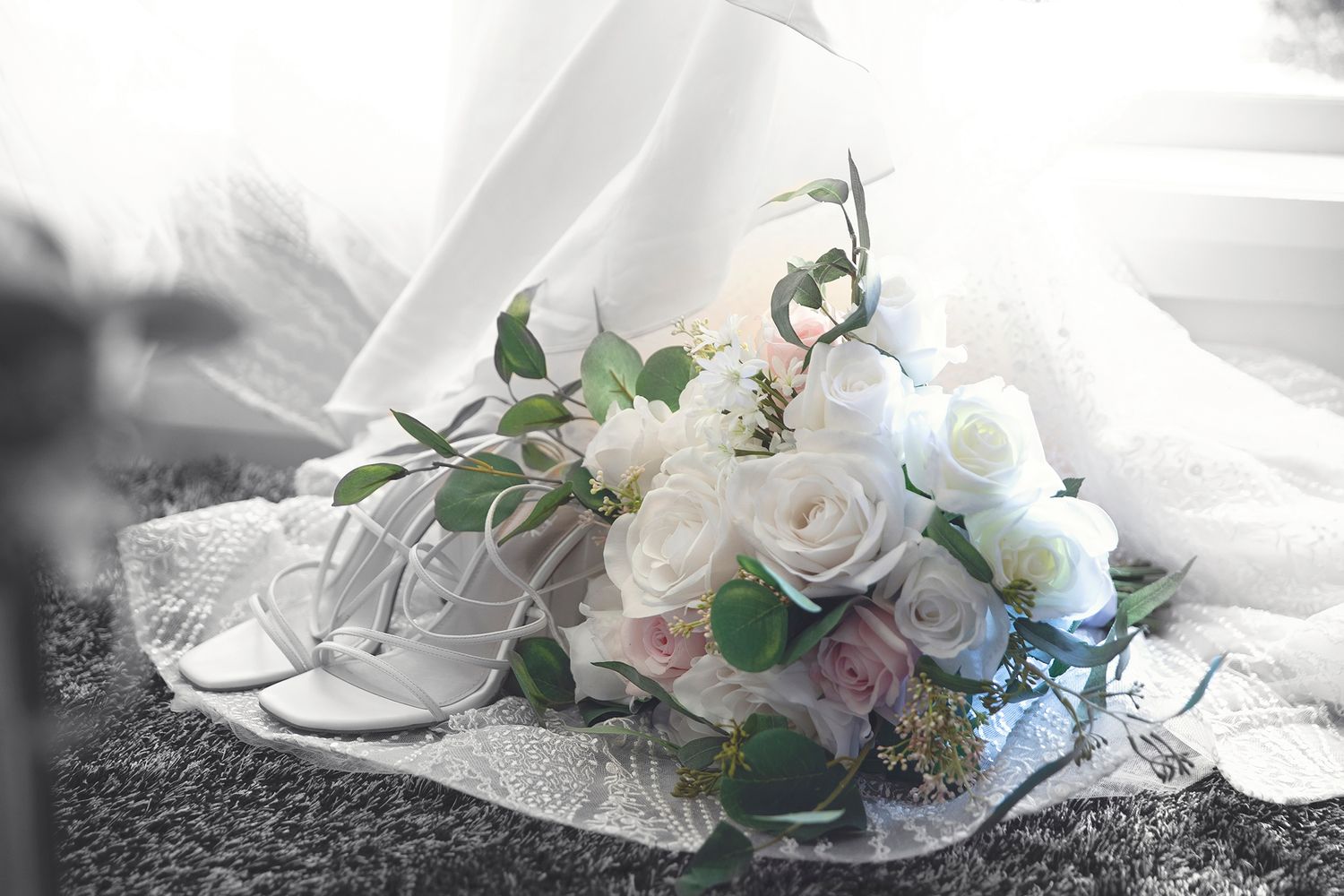 Bridal bouquet of white and pink roses beside lace wedding shoes.