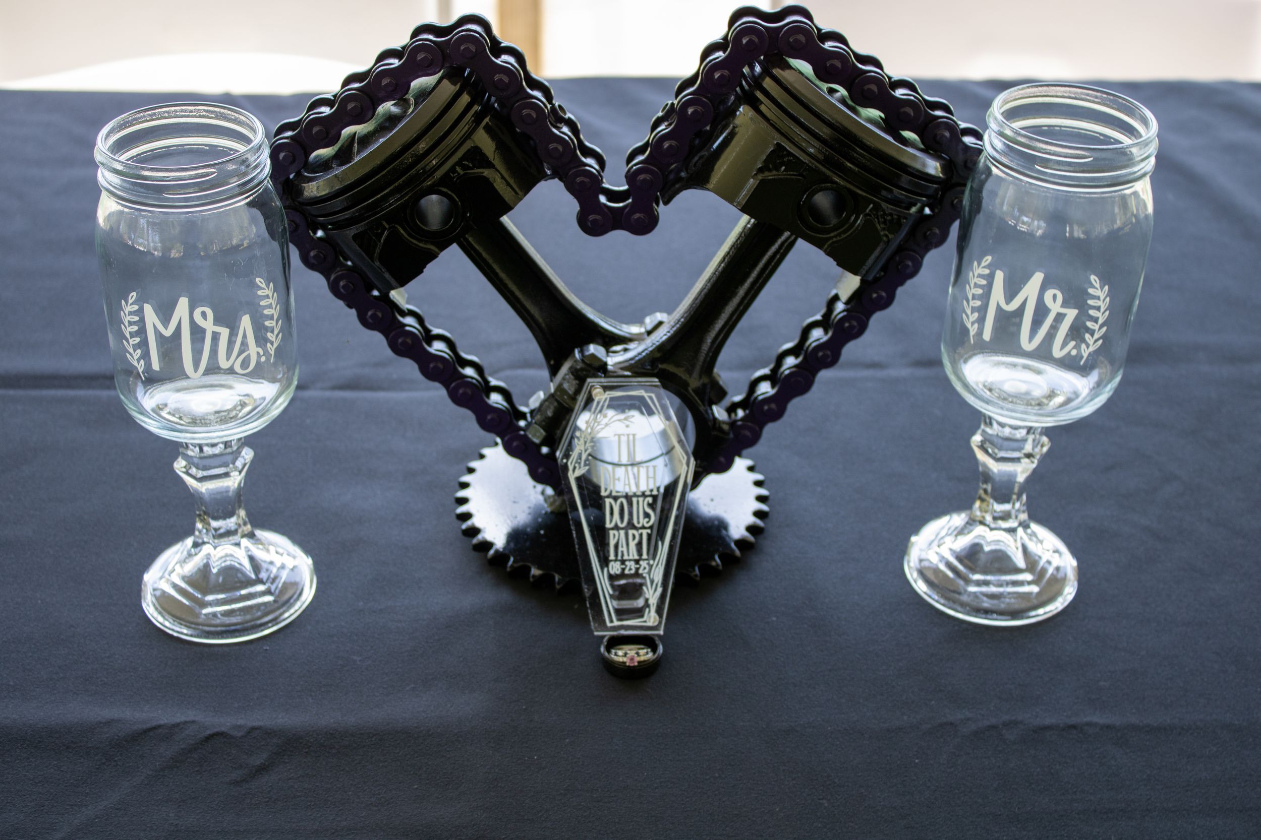 Gothic wedding table setting with black coffin decor and wine glasses on dark tablecloth.