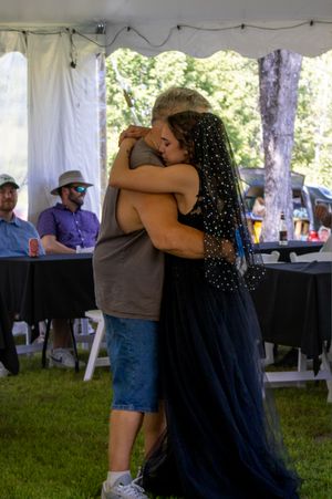People embracing under a white event tent during an outdoor gathering.