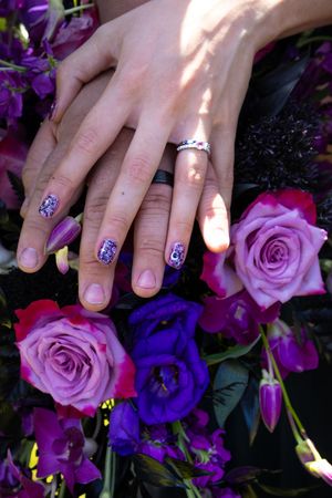 Close-up of hands with painted nails resting on purple and lavender roses in a floral arrangement.
