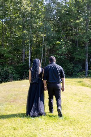 A couple walks together on a grassy hillside with trees and sunlight in the background.