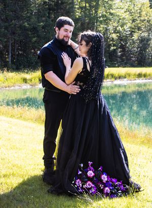 A couple shares an intimate moment in front of a turquoise lake surrounded by summer flowers and greenery.