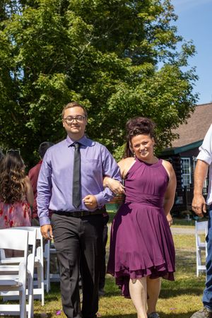 Wedding party members in purple and black attire gather outdoors on a sunny day.