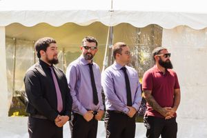 Wedding party members line up against white tent backdrop in formal attire.