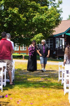 Outdoor wedding setup with white chairs and guests gathering on grass lawn.