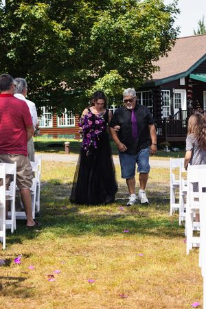 Wedding guests gather on a lawn with white chairs and a rustic building in the background.