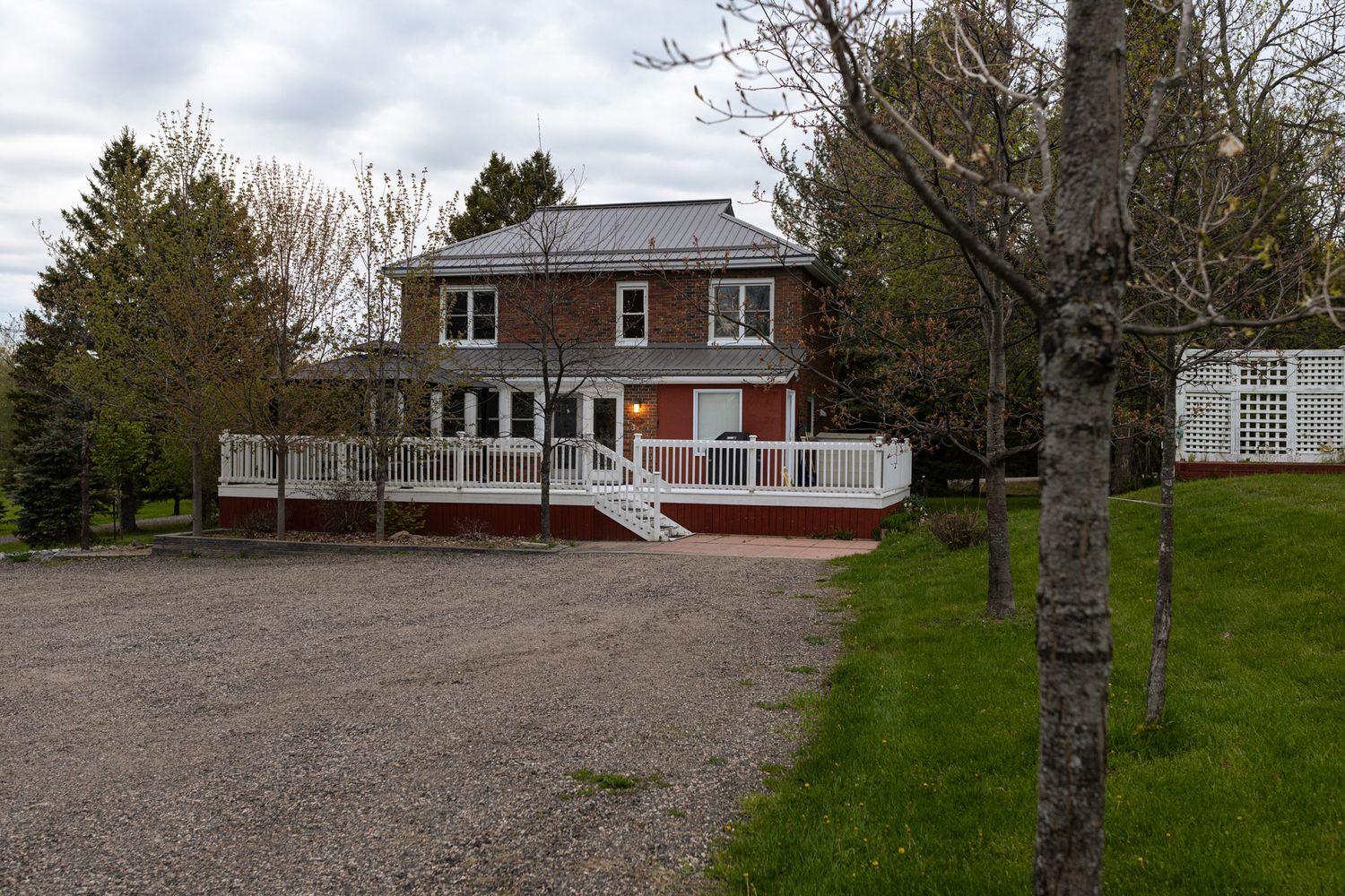 Red and white two-story house with front deck and gravel driveway.