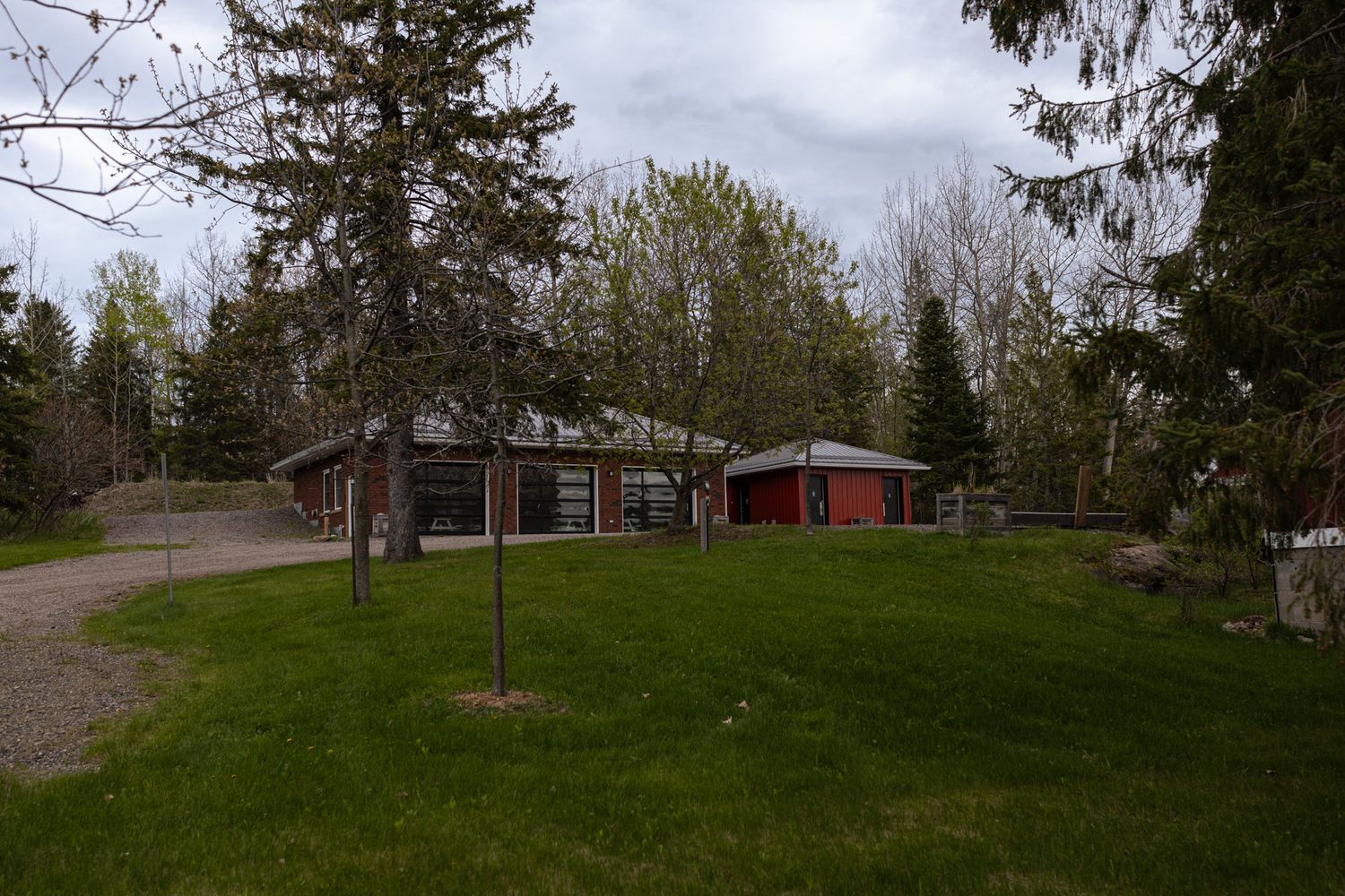 Ranch style property with red outbuilding on spacious green lawn surrounded by evergreen trees.