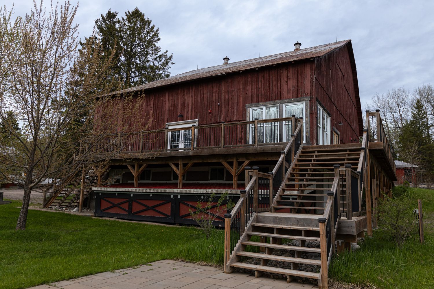 Weathered red barn with wooden staircase and covered lower level porch area.