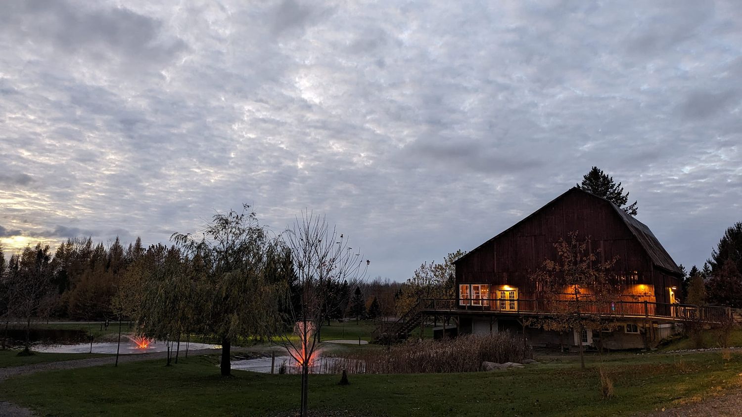 A rustic barn glows warmly at dusk against a cloudy sky.
