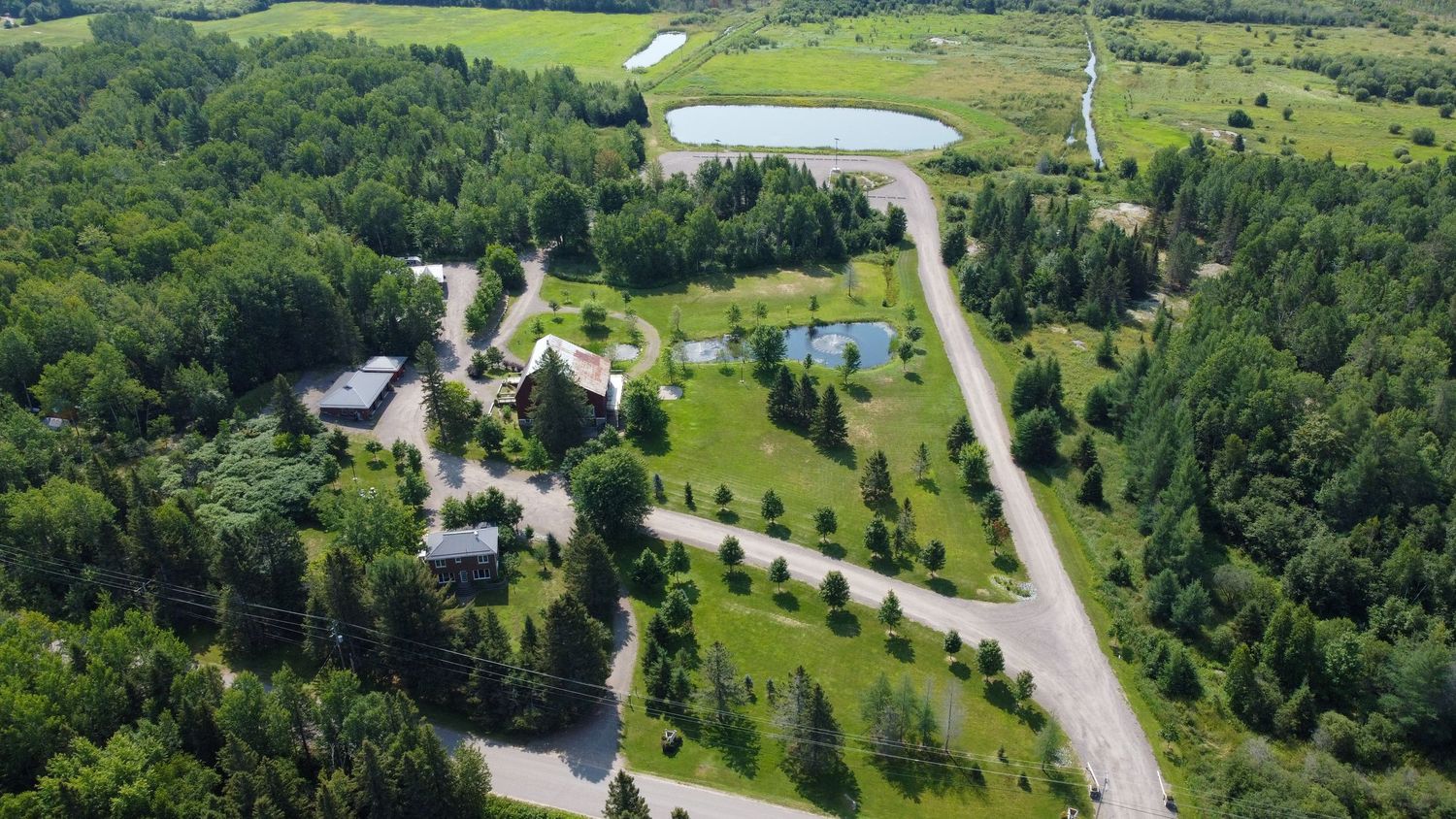 Aerial view of winding roads through a green wooded landscape with scattered buildings and small ponds.