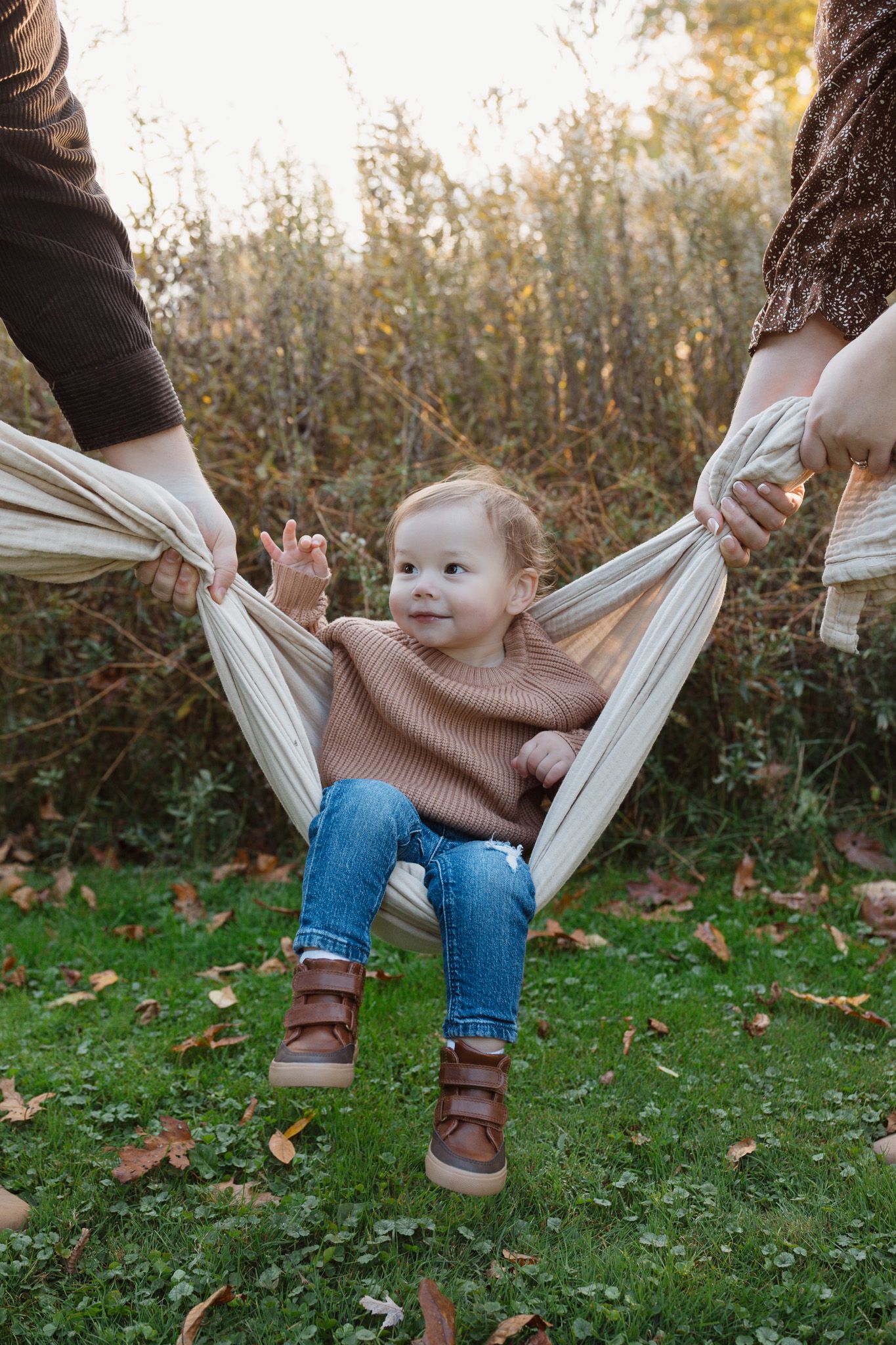 A young child is seated in a blanket held up by two adults.