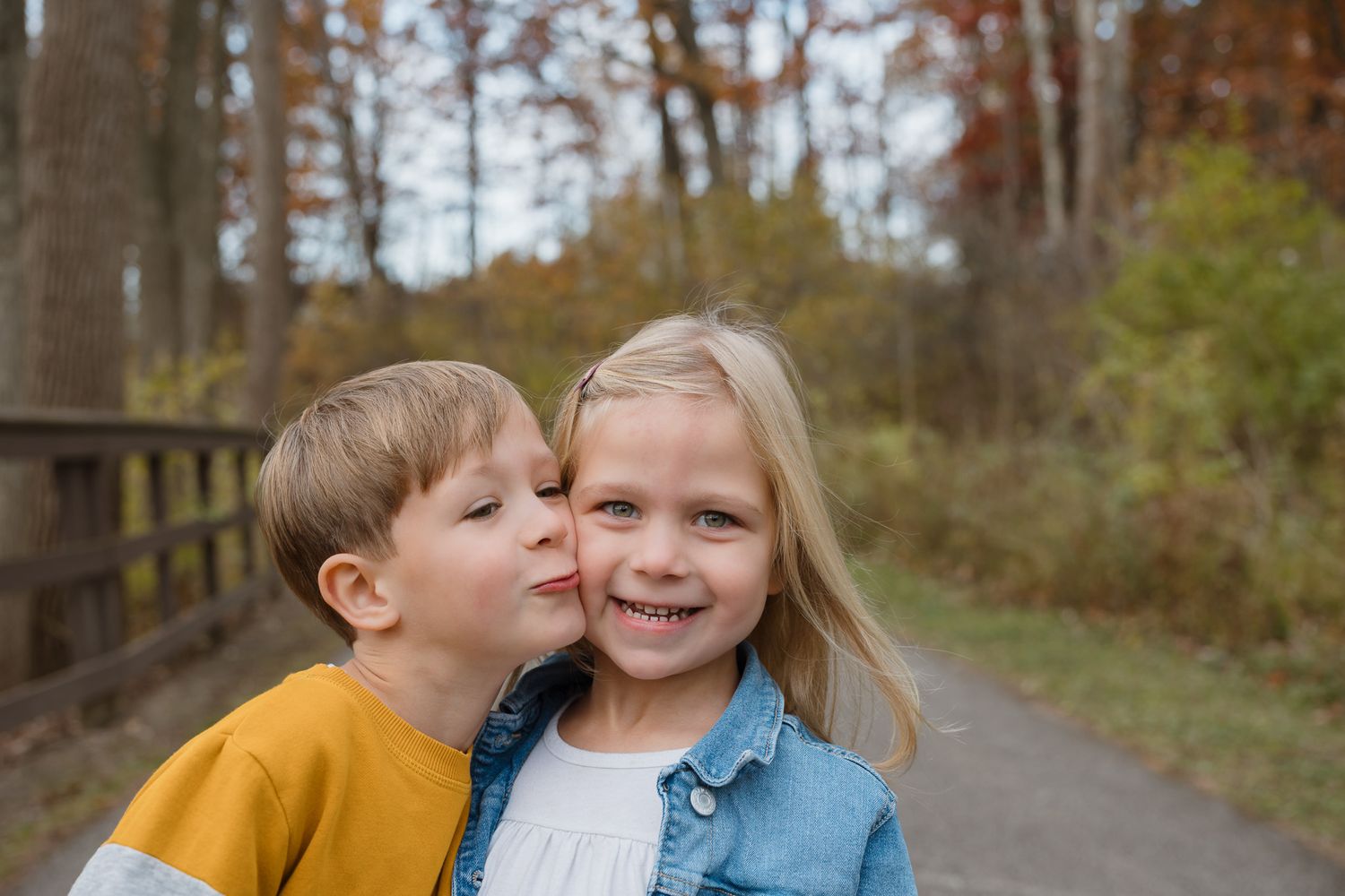 A young boy is kissing his sister on the cheek while they both smile into the camera.