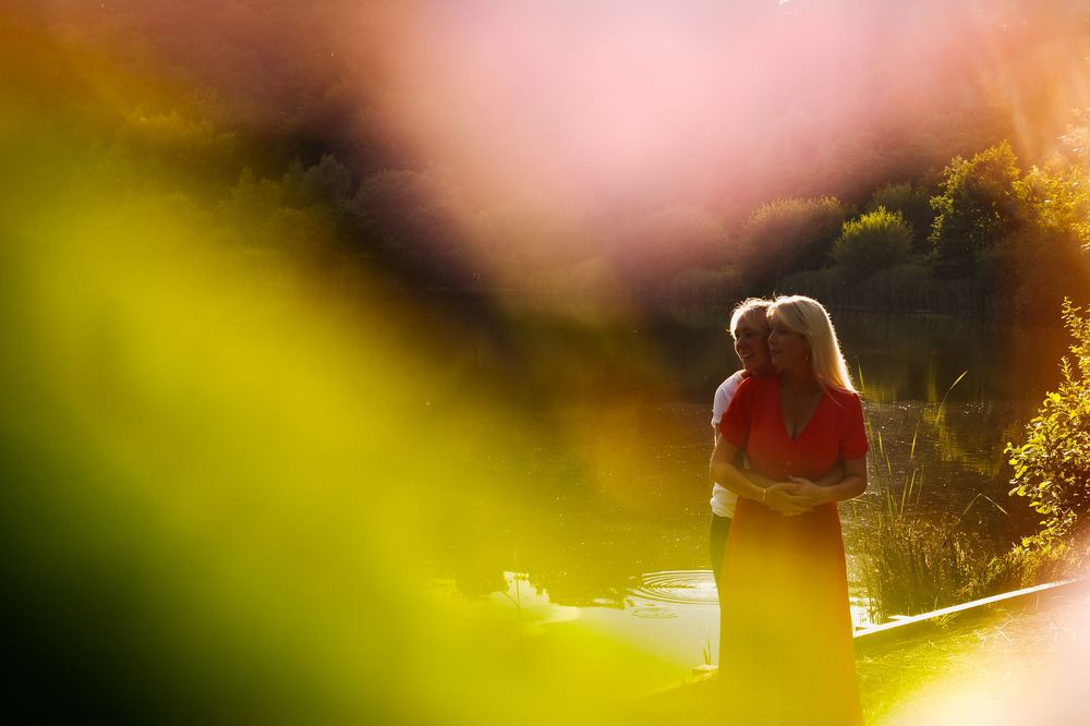 A silhouette figure in red stands in golden sunlight amid blurred green foliage at sunset.