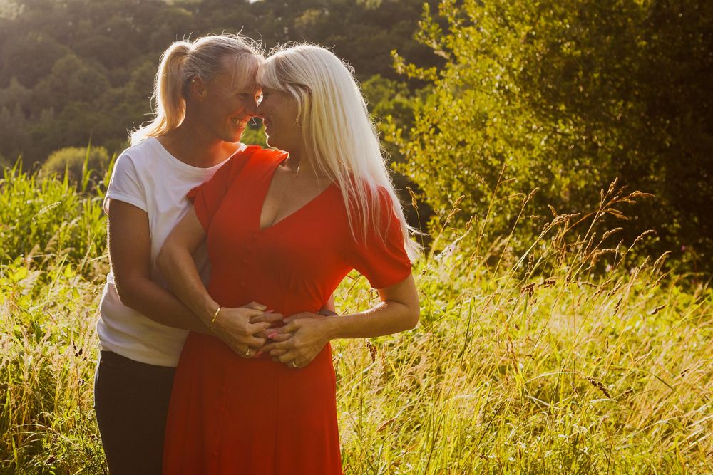 Sun-drenched couple in white and coral outfits share a tender moment in a golden grassy meadow.