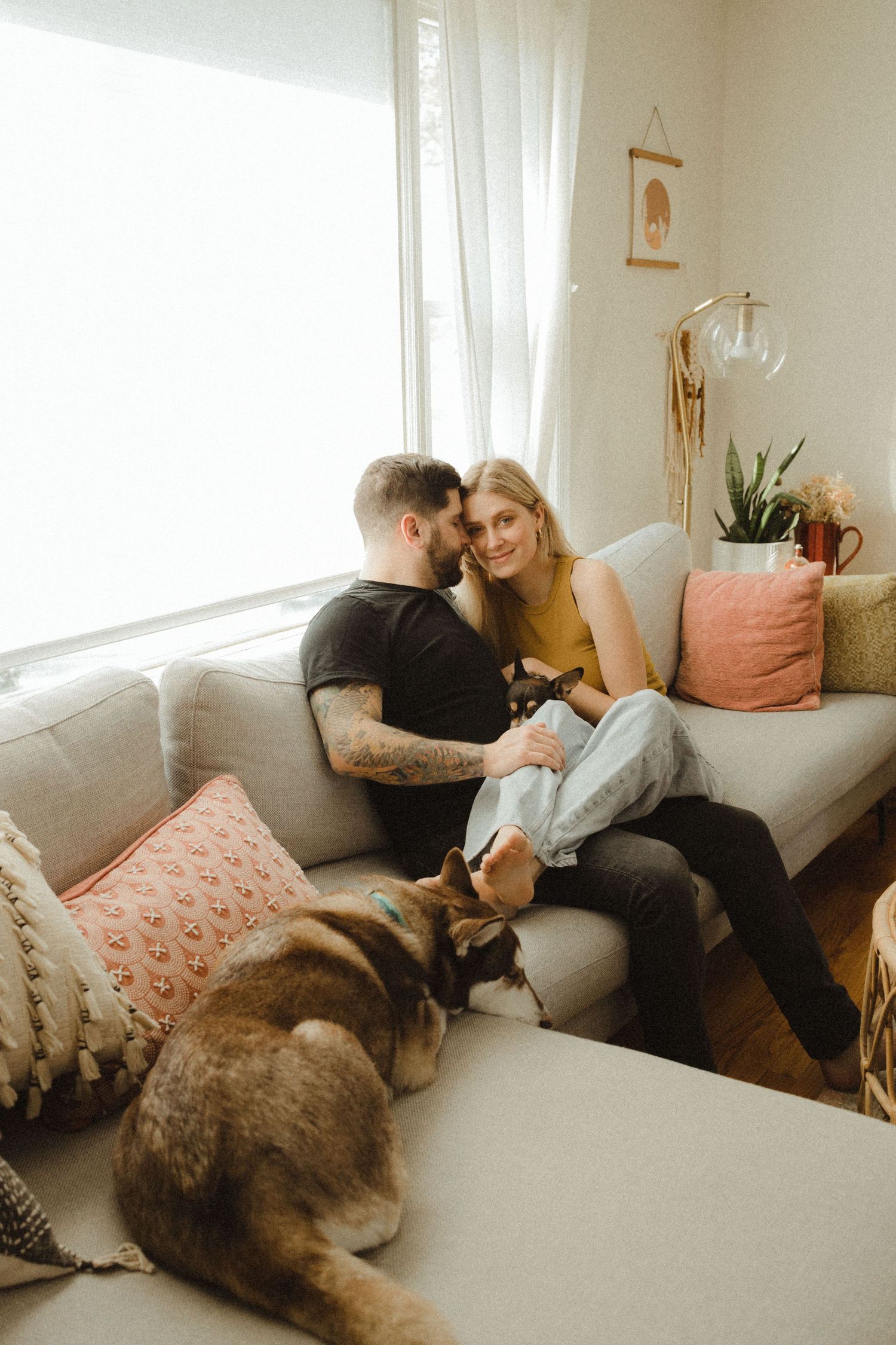 A couple relaxes on a tan sectional couch with their husky dog in a cozy living room with macrame decor in califon nj.
