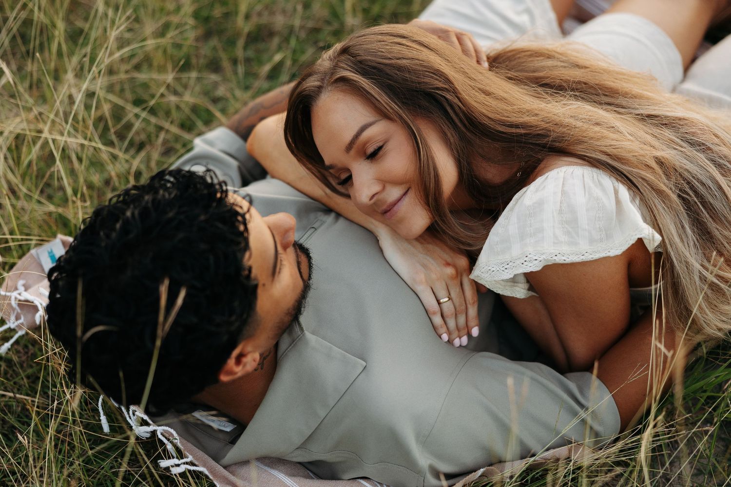 Couple lying in tall grass sharing intimate moment during outdoor photo session.